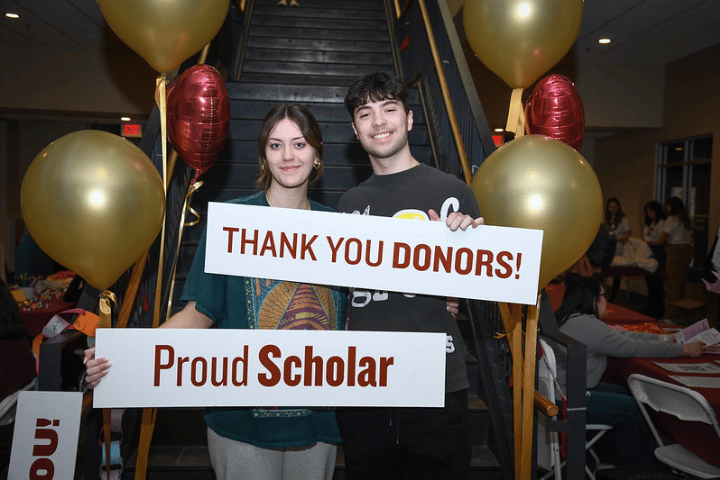 Two students holding signs saying Thank You Donors and Proud Scholar