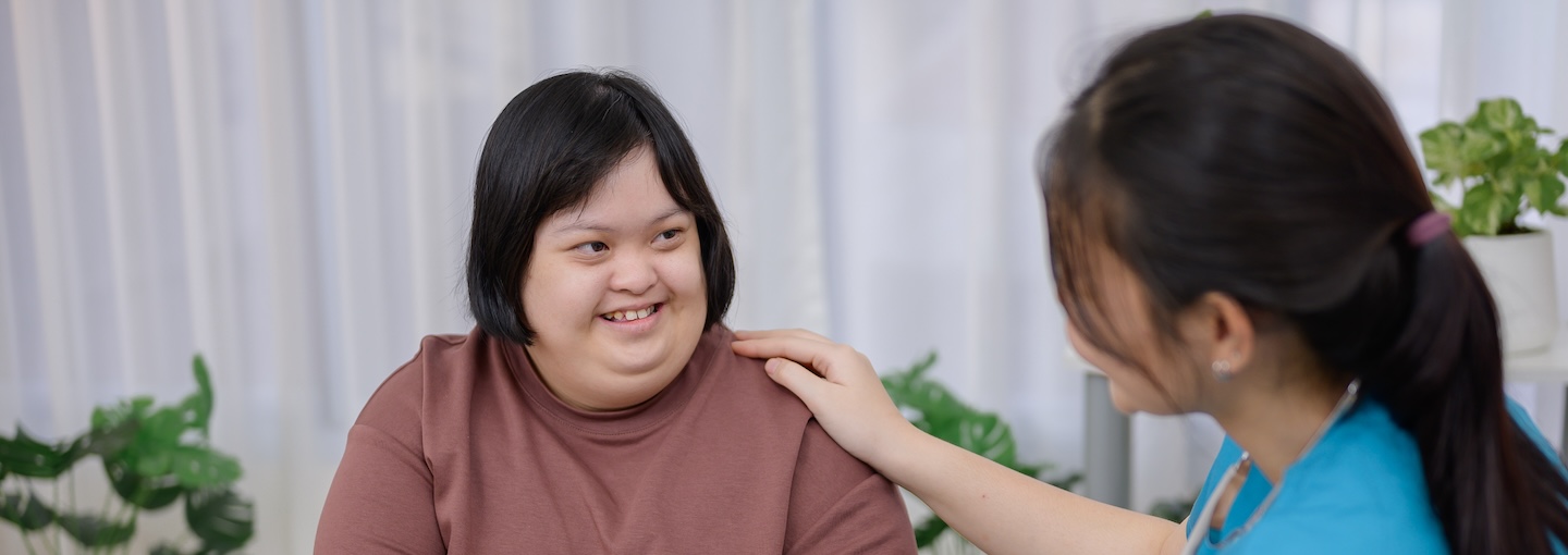 Nurse resting hand on shoulder of a girl with down syndrome and talking to her