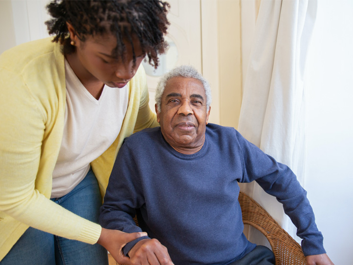 A home care assistant helps a man in a chair.