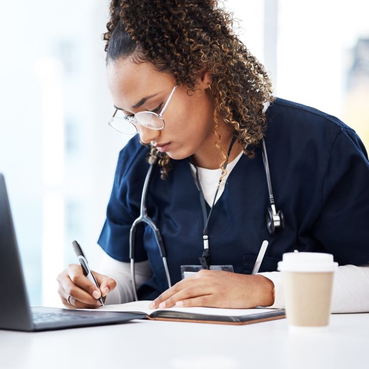 A nurse in front of a computer, writing in a notebook.