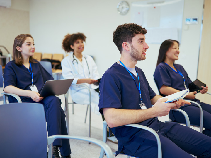 A group of nurses sit in chairs in a classroom.