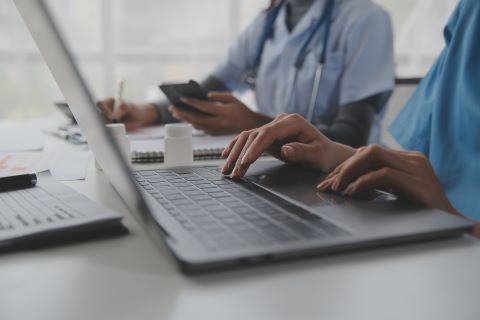 Two nurses one is on a laptop and one is using a mobile phone.