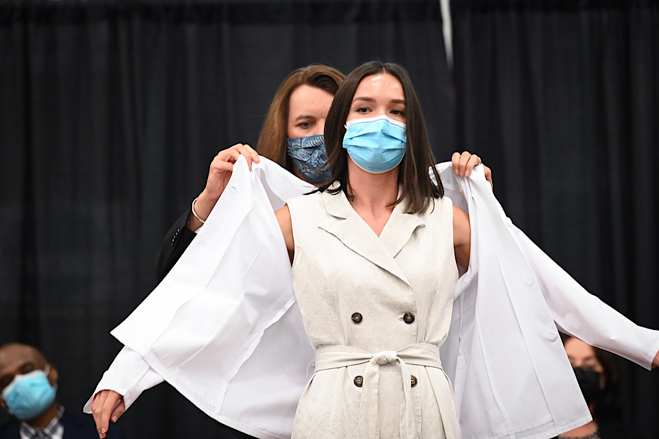 Dean Christine Birnie puts a white coat on a first-year pharmacy student.