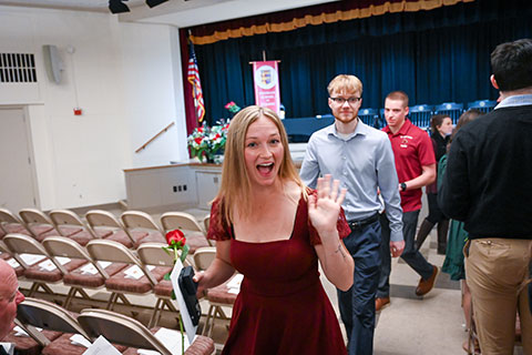 A smiling graduate prossesses down the aisle.