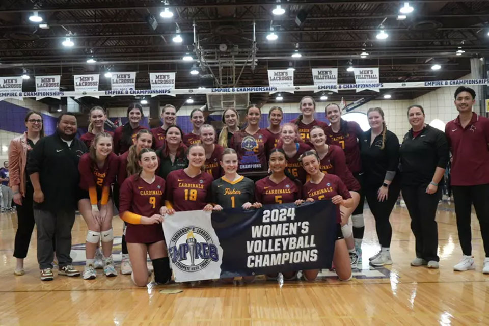 The women's volleyball team holds up the Empire 8 Championship banner.