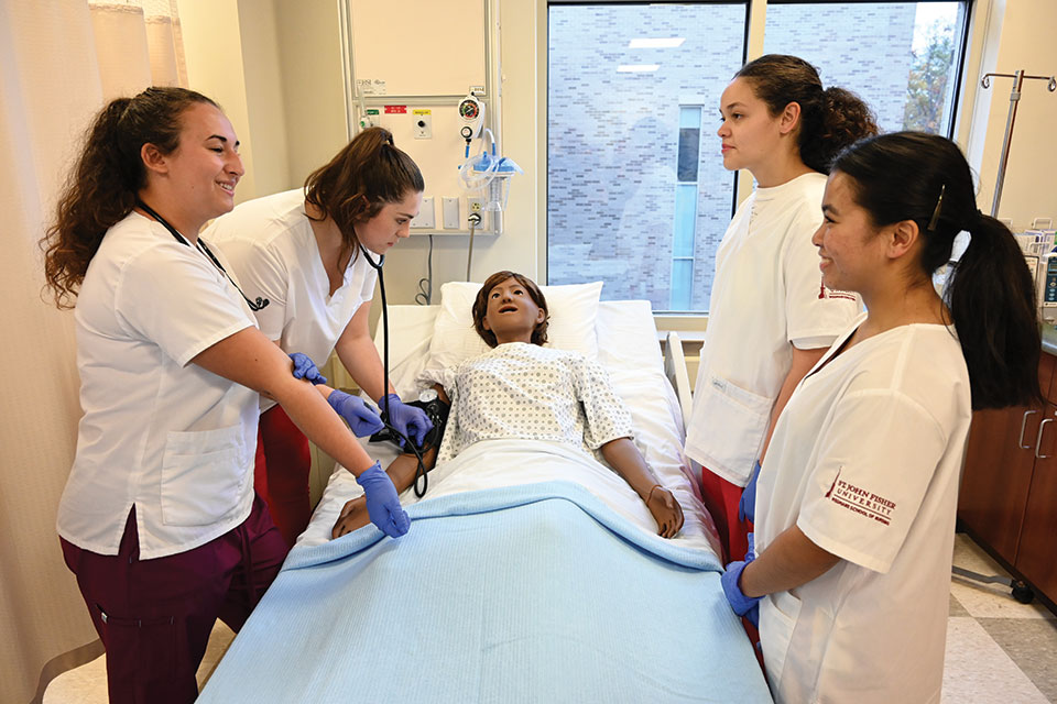 Four nursing students learn skills on a mannequin in the SIM Lab.