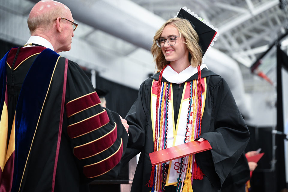 A graduate shakes hands with President Rooney during Commencement.