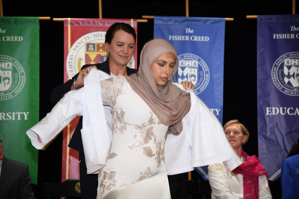 Dean Christine Birnie helps a student put on their white coat.
