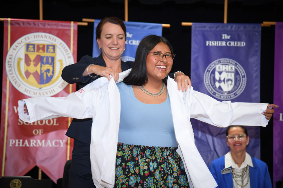 Dean Christine Birnie helps a student put on their white coat.