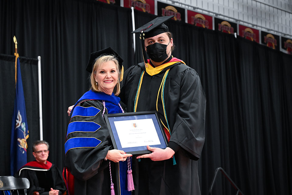 Dean Tricia Gatlin presents graduate Athan Brown with a Trustees Ranking Scholar Award.