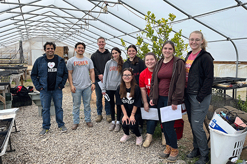 Students pose with gardening tools in a greenhouse.