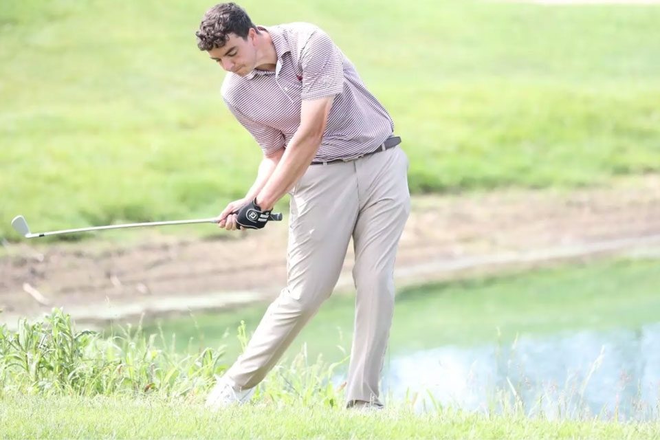 A member of the men's golf team swings at the ball.
