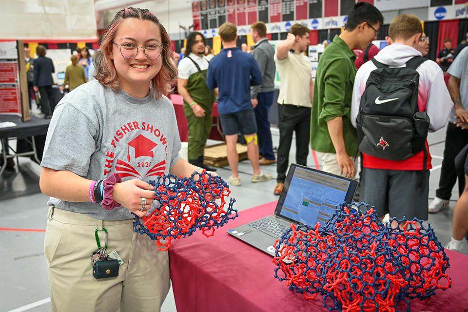 A student holds objects on display as part of a presentation at the Fisher Showcase.