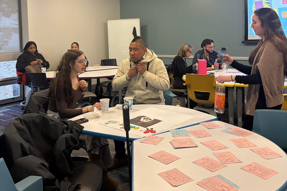 Students gather around tables to practice Spanish conversation at Cafecito event.