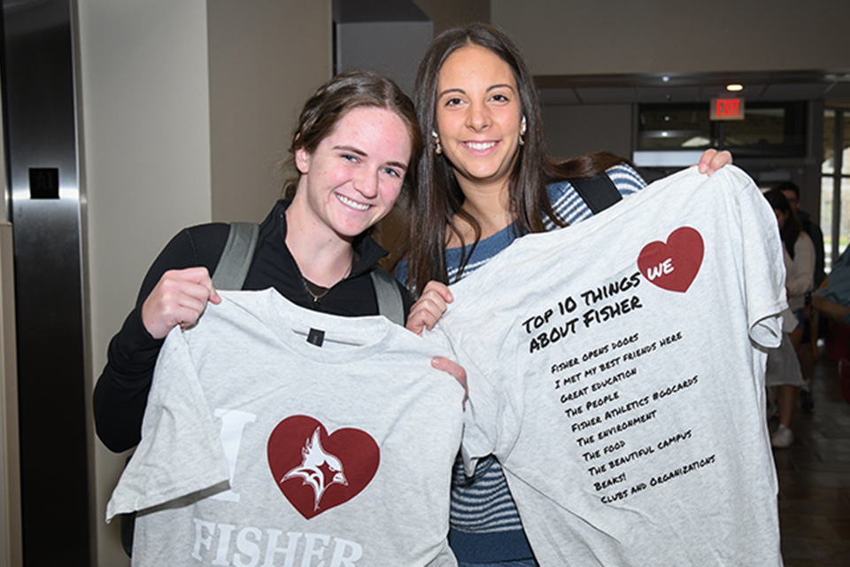 Students hold up t-shirts from I Heart Fisher Giving Day with Ten Things we Love About Fisher.