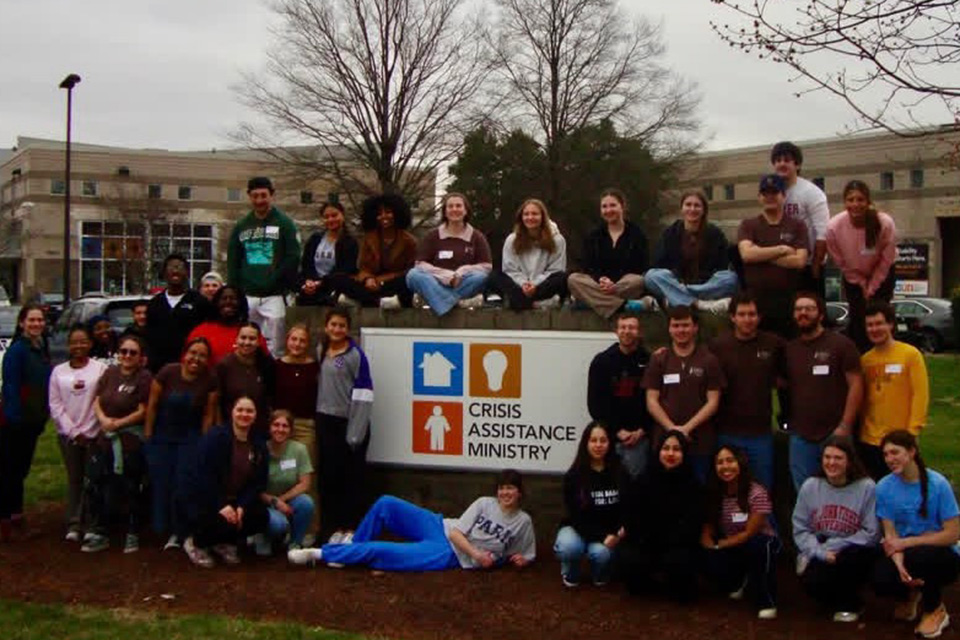Campus Ministry students during Spring Break at the entrance sign for Crisis Assistance Ministry.