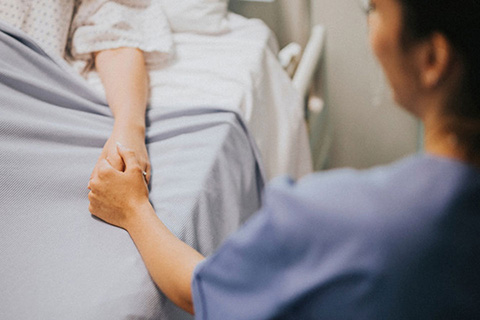 A nurse sitting and holding the hand of a patient in a hospital bed.