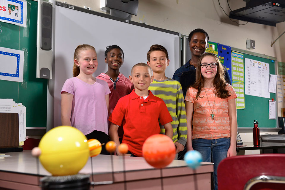 A teacher and students in front of a smartboard.