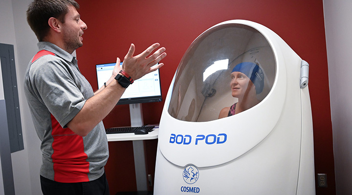 A professor demonstrates the use of the BODPOD in the Athletic Performance Lab.