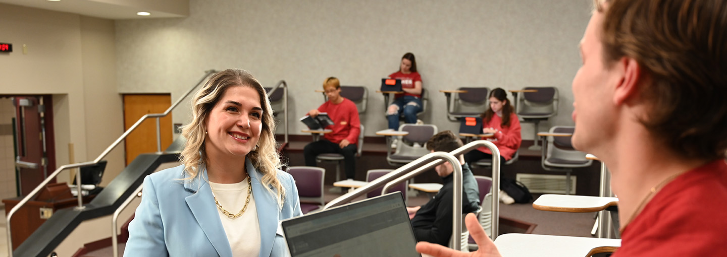 A student converses with a faculty member in a classroom setting.