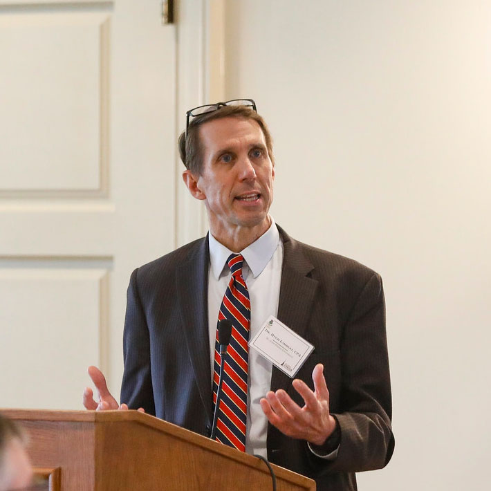 Dr. Hugh Lambert presenting from a podium.