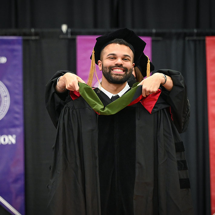 A pharmacy graduate is hooded at the Pharm.D. ceremony.