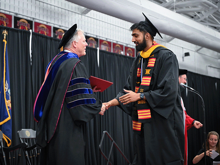 A student shakes hands with a professor while receiving his diploma at Commencement.