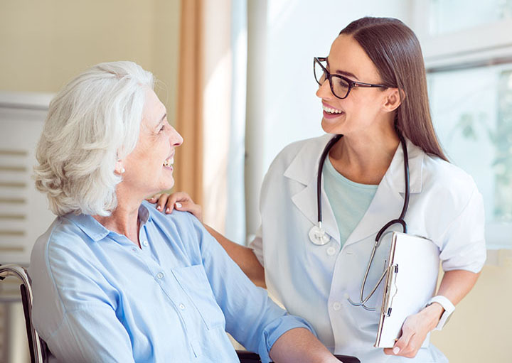 Young nurse with clipboard speaks to a white-haired smiling woman.