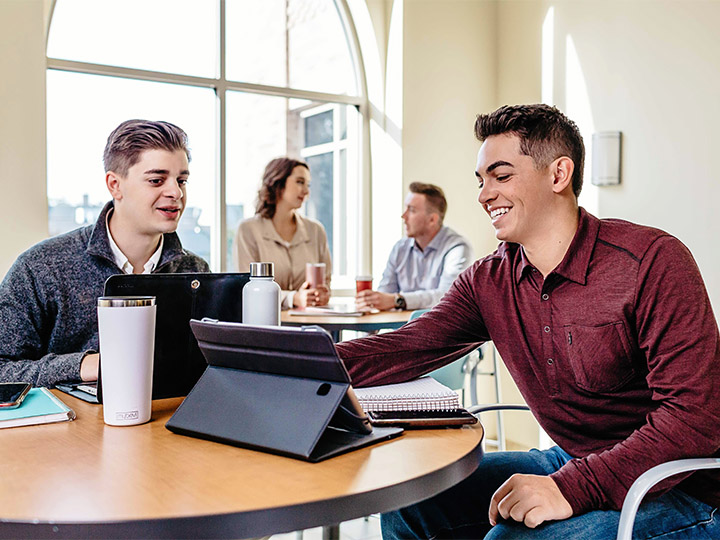 Two students talk over a tablet computer.