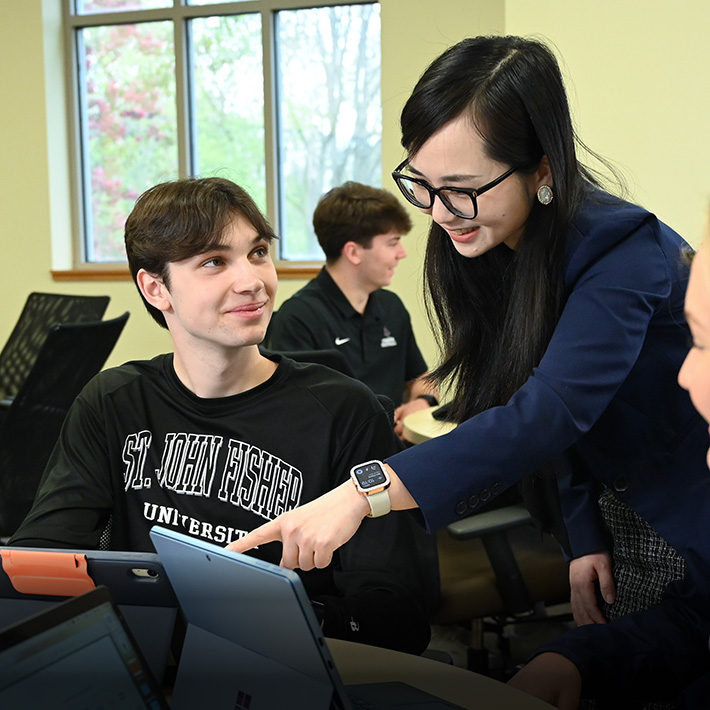 A business professor provides assistance to a student working on an iPad.