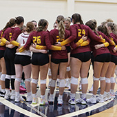 The Fisher womens volleyball team huddles together with arms linked.