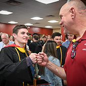 An athletic trainer fist bumps a student athlete at commencement.