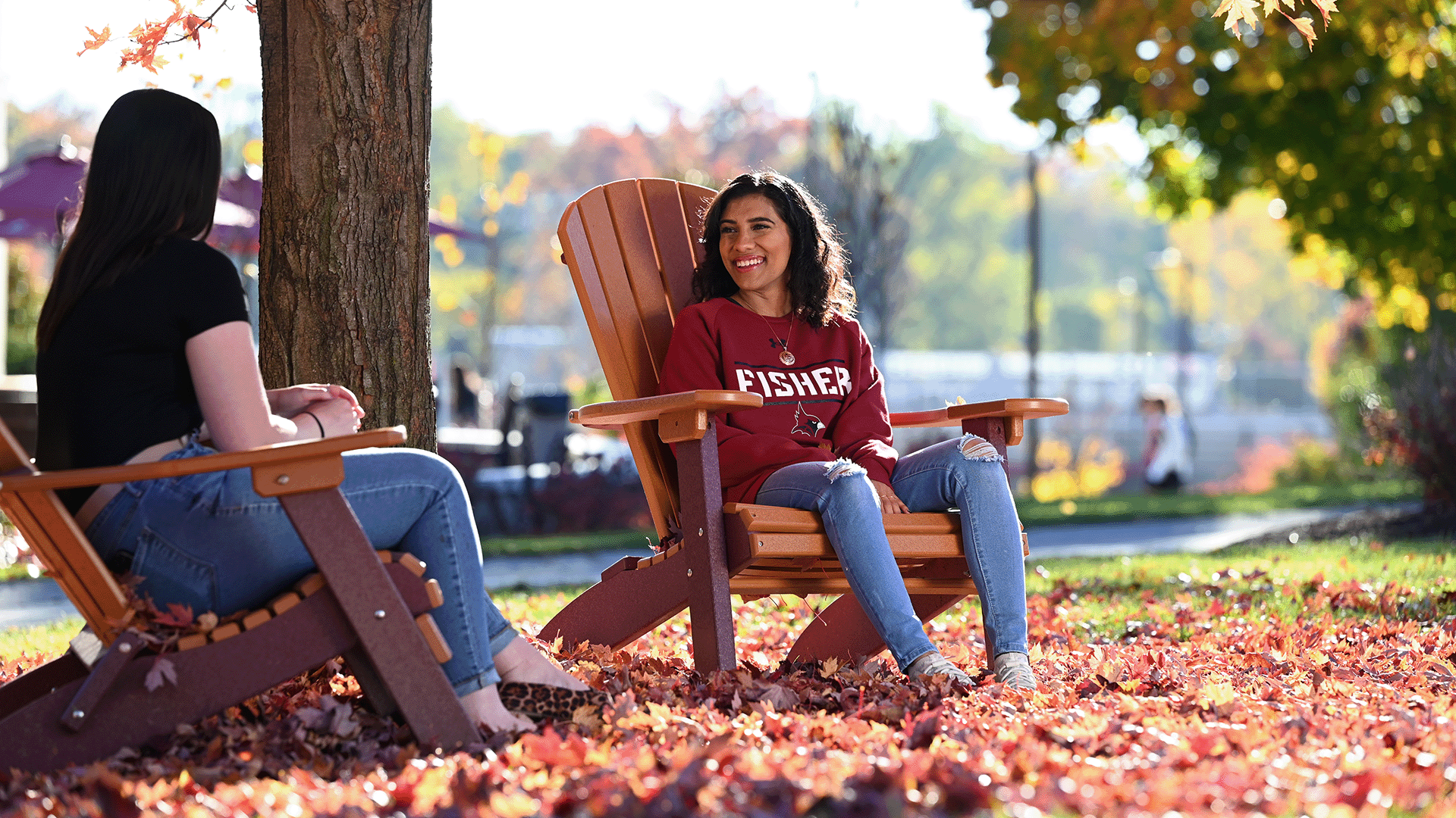 Students sit in Adirondack chairs in the leaves on campus.