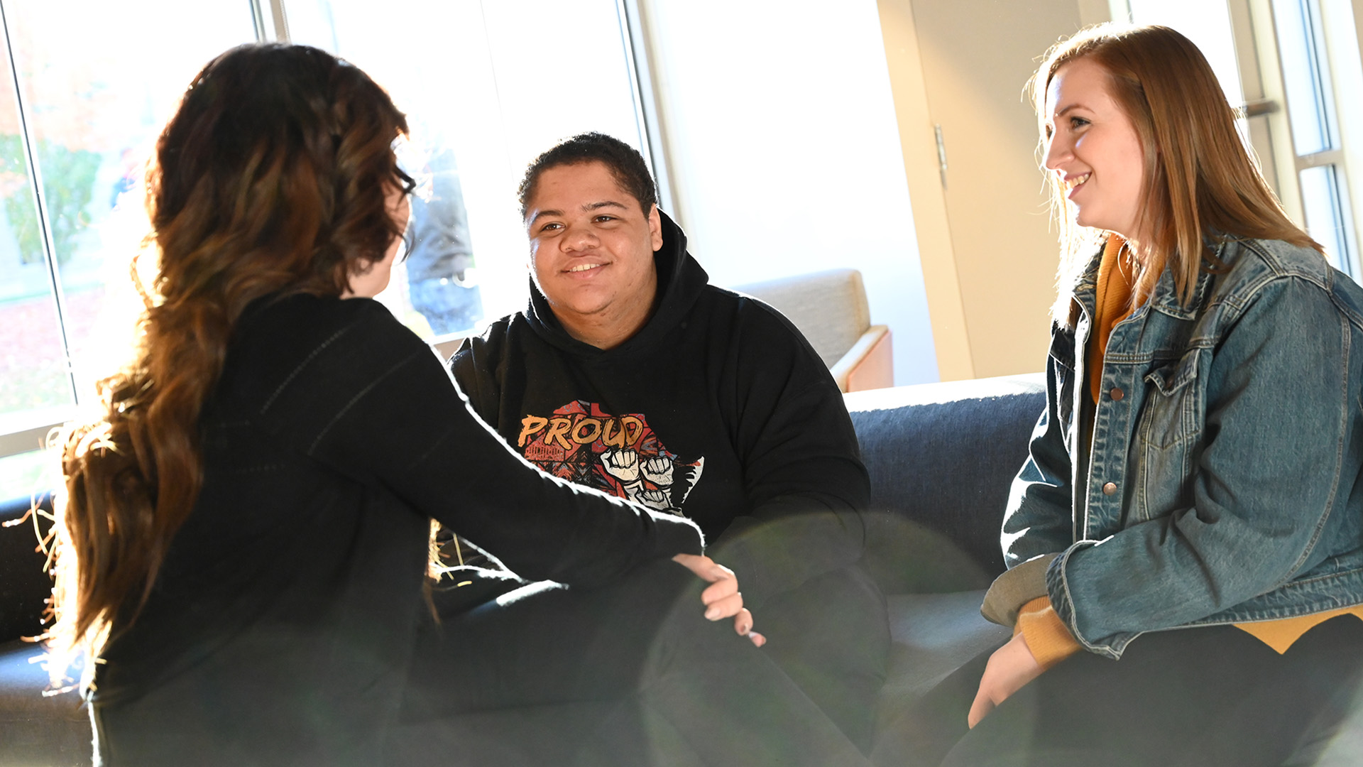 A group of students sit together in the campus center with the sun shining through the windows.