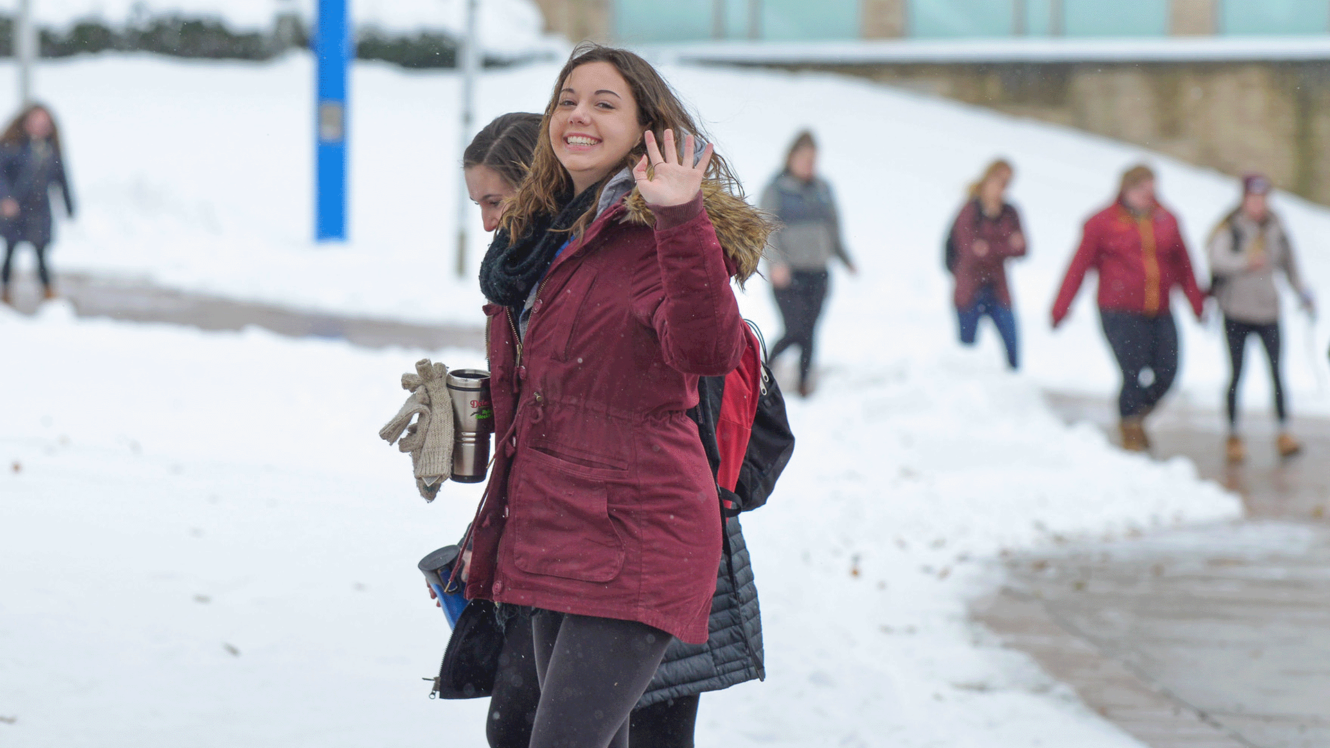 A student waving happily on Fisher's campus in the winter.