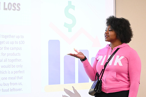 A student gives a presentation while gesturing to a dollar symbol during business camp.