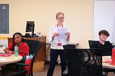 A professor talks with seated students during business camp.