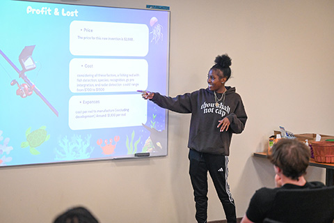 A student gives a presentation while gesturing to slide during business camp.