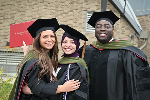 Graduates stand together in Commencement regalia.