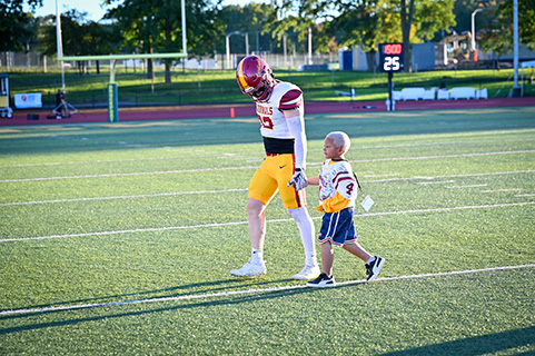 A player walking hand in hand with a Camp Good Days camper.