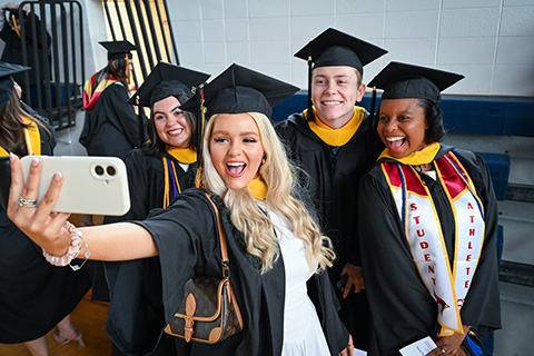 Students take a selfie in commencement regalia.