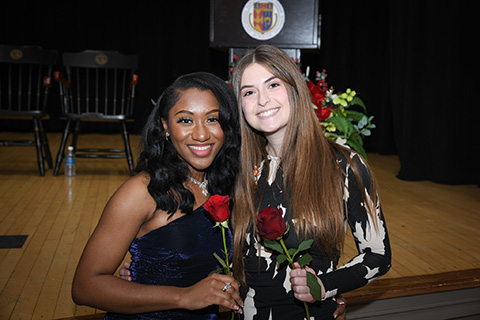 Graduating nursing students stand together at the stag holding roses.