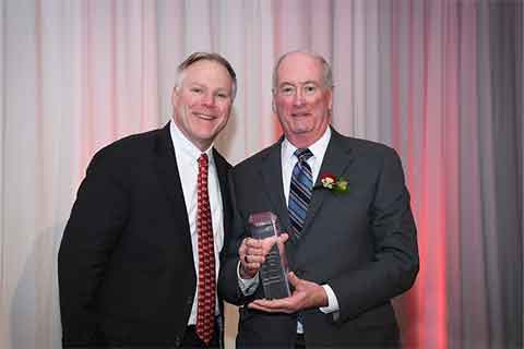 One person holding an award and standing with another individual