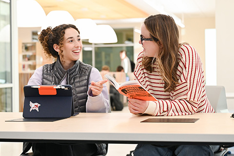 A student using an iPad in Lavery Library while sitting with another student.