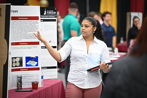 A student shares her research on a poster at the Fisher Showcase.