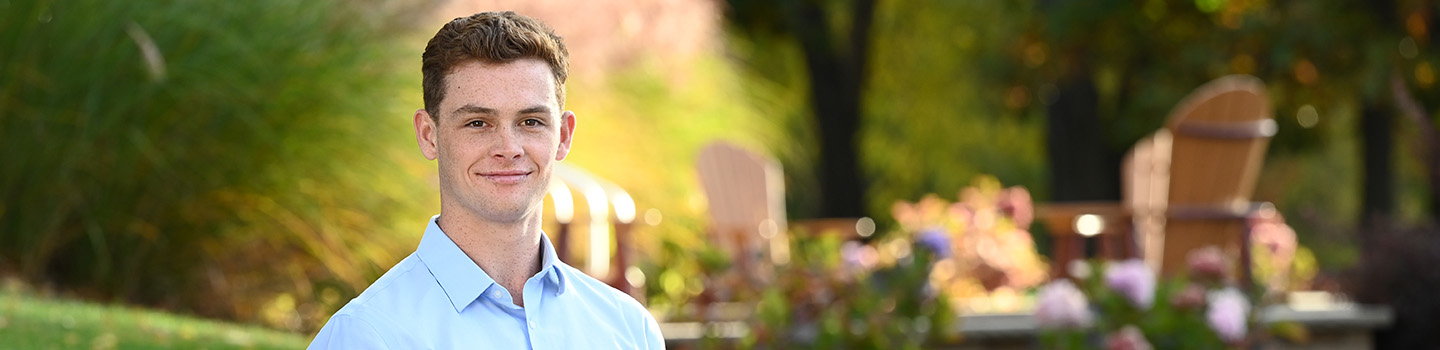 A graduate business student stands near the edge of the School of Business on campus at Fisher surrounded by fall foliage.