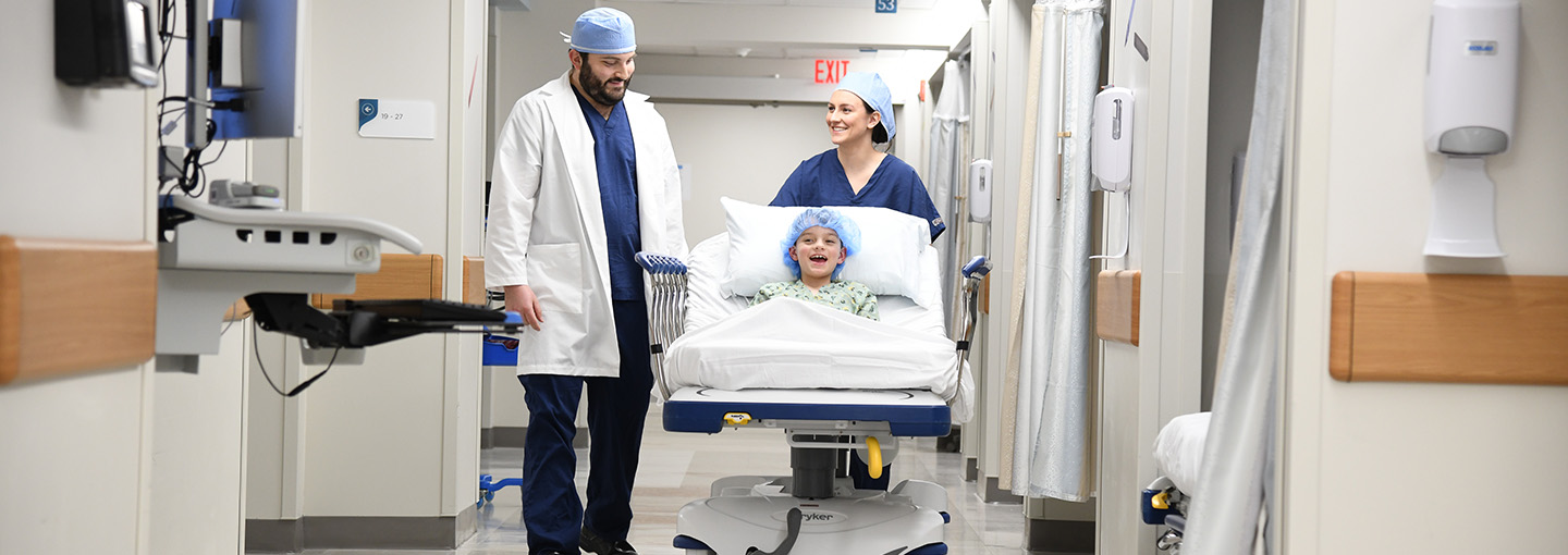 Nurse anesthetists walk through a hospital corridor with a patient on a bed.