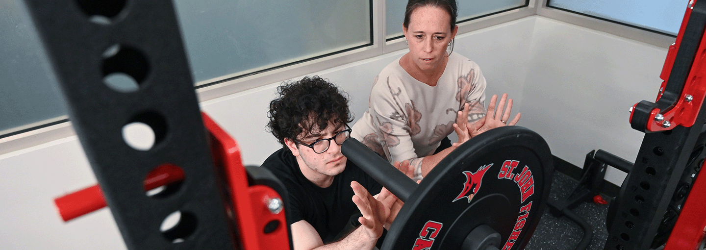 A professor models how to spot for a weightlifter in the athletic performance lab.