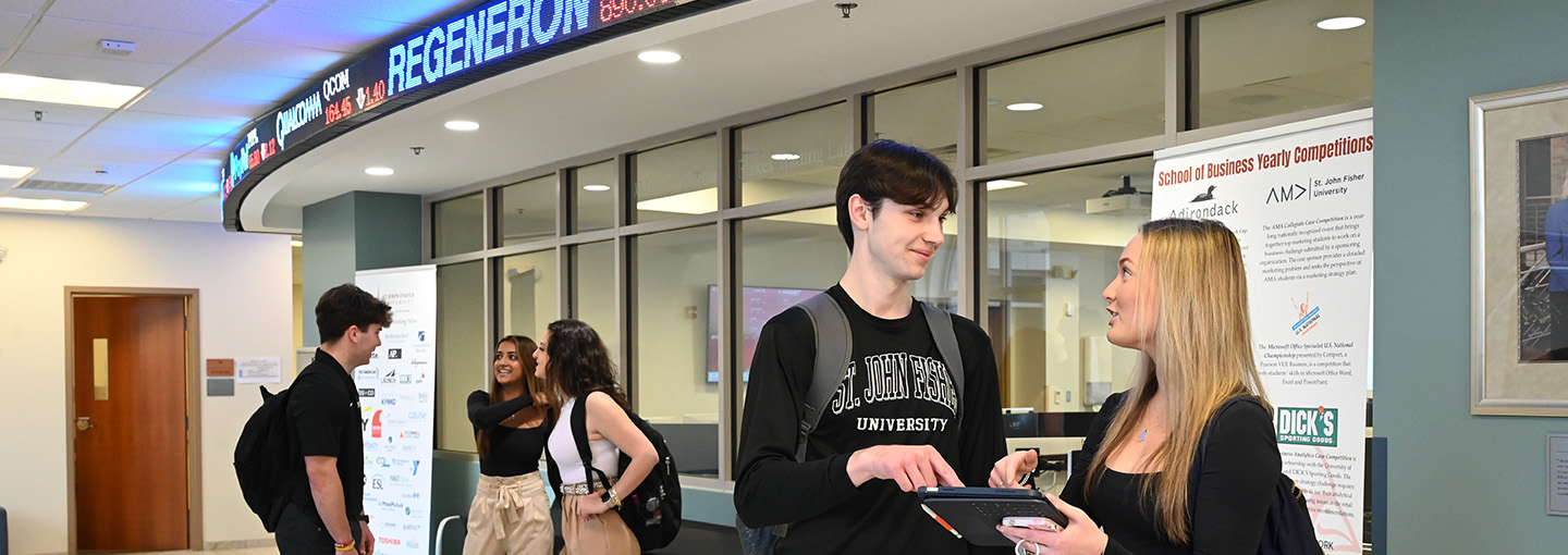 Students in the School of Business mingle together with the trading lab in the background.