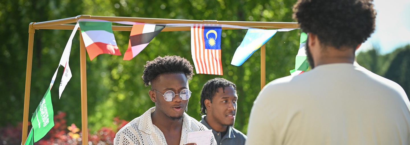 A student visits a booth with flags representing multiple countries at the Inclusion Dinner event at Fisher.